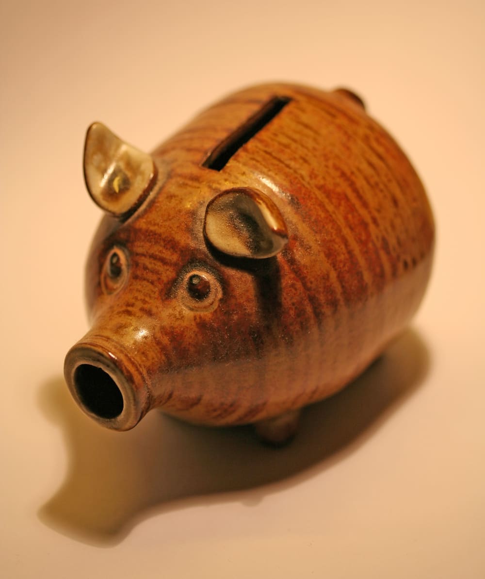 A glazed brown pottery piggy bank with a coin slot on its back